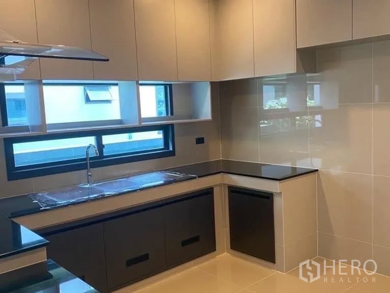 Detached House for rent in Bang Kapi, Bangkok - Built-in kitchen with L-shaped black countertops, glossy cabinets and window above sink.