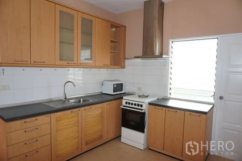 Condominium for rent in Watthana, Bangkok - Separate kitchen with wood cabinetry, sink, oven, range hood and side window for ventilation.