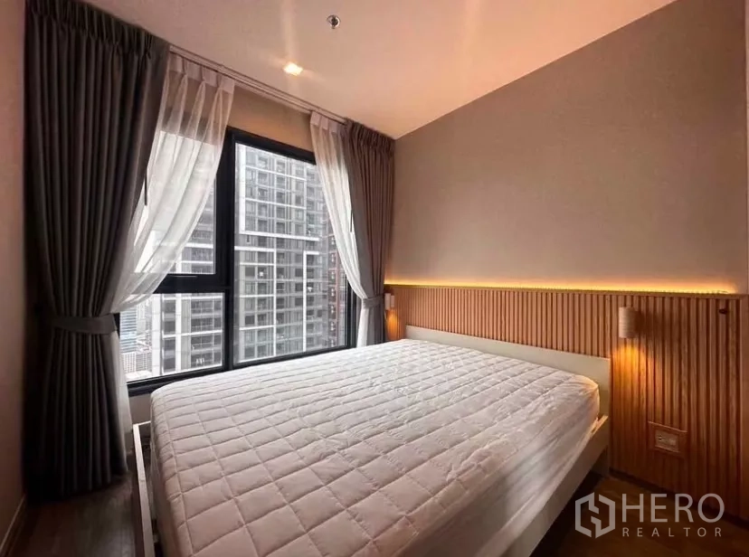 Condominium for rent in Chatuchak, Bangkok - Primary bedroom with large windows, bedside lighting, and city view.