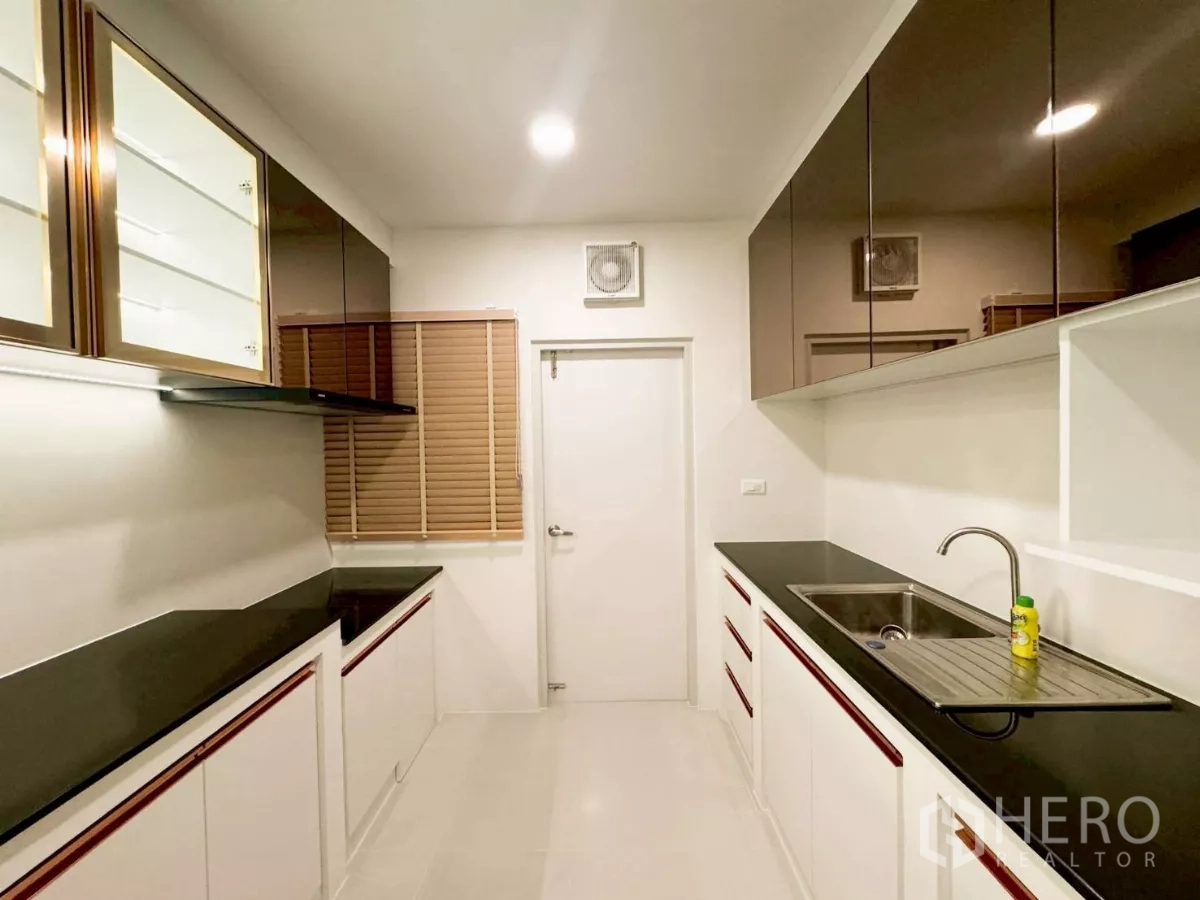 独立式住宅 出租在Bang Phli, Samut Prakan - 封闭式厨房，黑色台面、白色橱柜、不锈钢水槽与充足收纳。