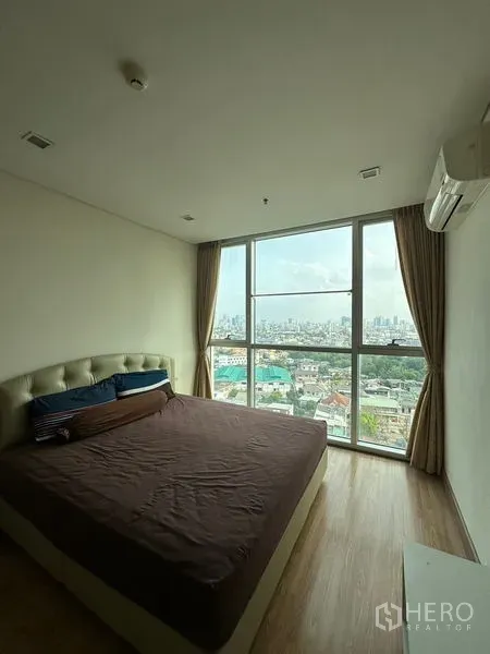 Condominium for sale in Watthana, Bangkok - Bedroom with floor-to-ceiling window and panoramic Bangkok skyline view.