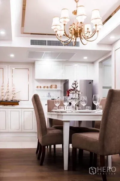 Condominium for rent in Huai Khwang, Bangkok - Dining area with chandelier, four upholstered chairs and classic white cabinetry in the background.