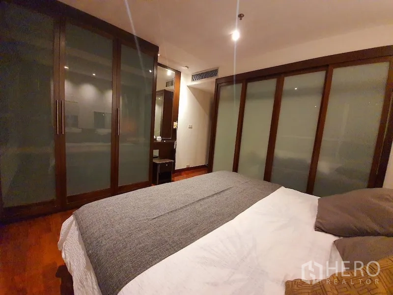 Condominium for rent or sale in Pathum Wan, Bangkok - Bedroom view showing extensive frosted sliding wardrobes and a dressing nook.