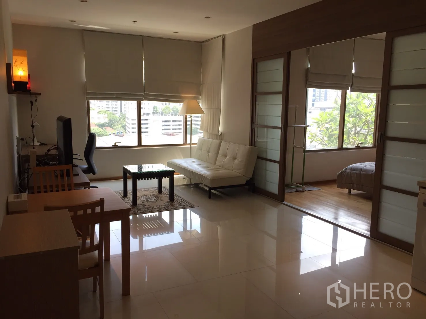 公寓 出租或出售在Khlong Toei, Bangkok - 开放式起居区，配电视与餐桌，亮面地砖，推拉门通往卧室及城市景观。