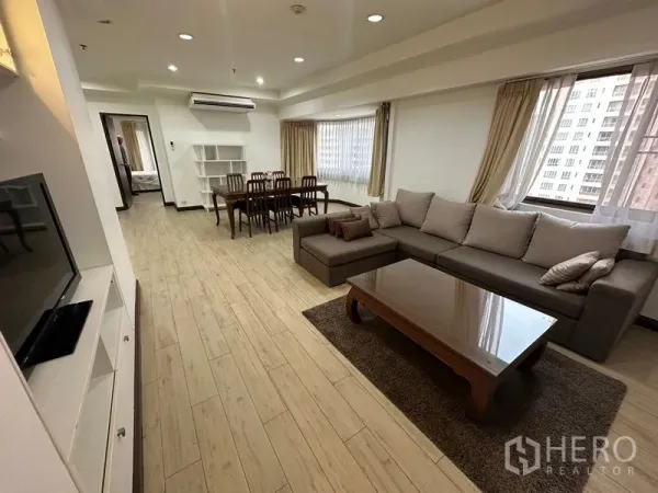 Condominium for rent in Watthana, Bangkok - Open-plan living and dining area with L-shaped sofa, TV console and wood-look floors in Watthana, Bangkok.