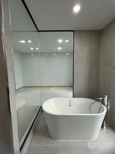 Detached House for rent or sale in Suan Luang, Bangkok - Freestanding bathtub next to a floor-to-ceiling glass partition in a neutral-toned bathroom