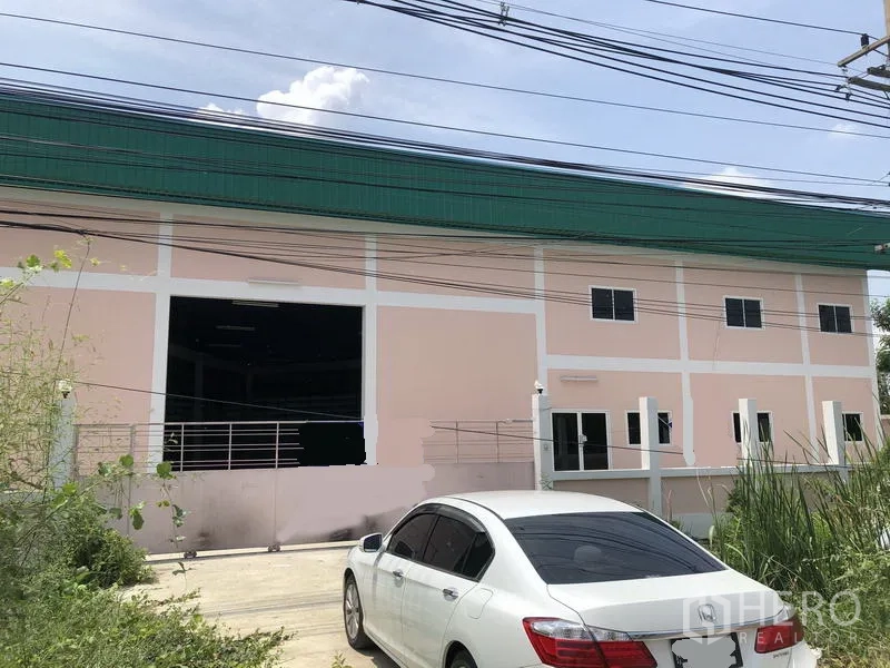 Factory for rent in Pathum Thani - Street-facing factory facade with large loading bay, multiple windows, and on-site parking area.
