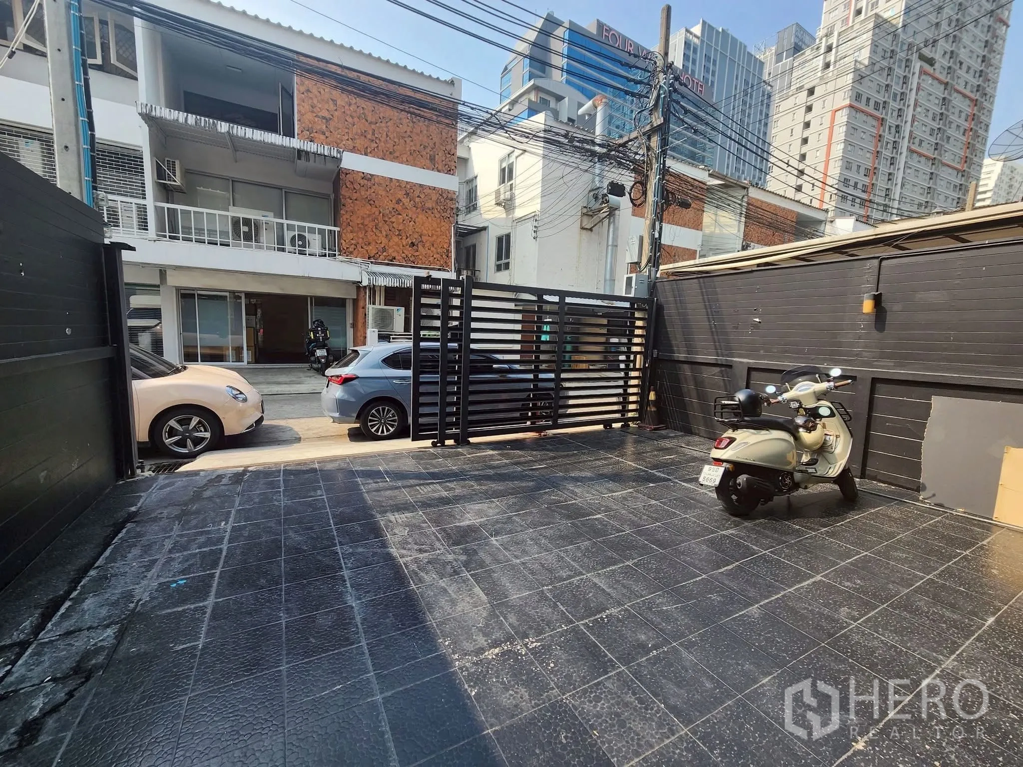 โฮมออฟฟิศ for rent in Khlong Toei, Bangkok - ทางเข้าบ้านพร้อมลานกระเบื้องและสกู๊ตเตอร์ มองออกไปยังอาคารเตี้ยและตึกสูงในเมือง