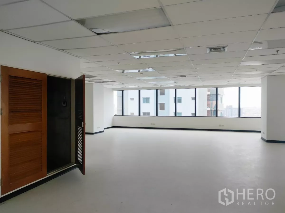 办公空间 出租在Huai Khwang, Bangkok - 空置办公室内景，白墙、长窗与格栅吊顶，入口旁设木质设备柜。