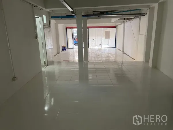 店屋 出租在Watthana, Bangkok - 店屋一层开放式空间，白色地砖、承重柱及朝街的大幅玻璃门面。