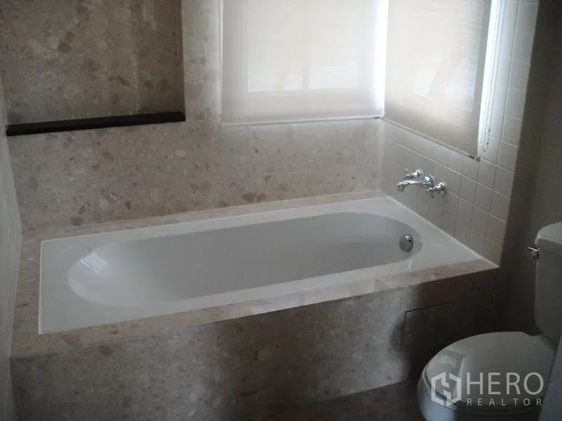 Detached House for rent in Wang Thonglang, Bangkok - Bathroom featuring a built-in bathtub, stone tiles and a frosted window.