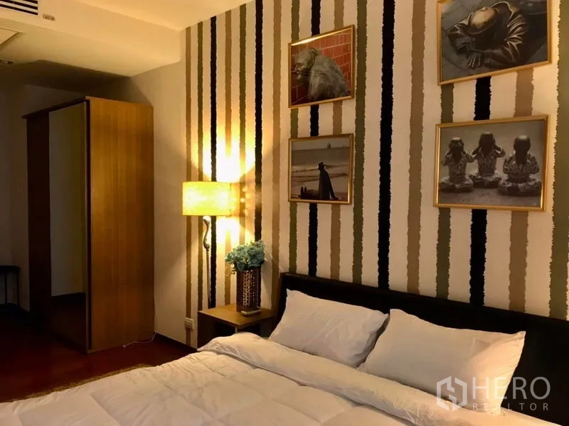 公寓 出租在Watthana, Bangkok - 卧室挂有装饰画，条纹特色墙与柔和灯光。