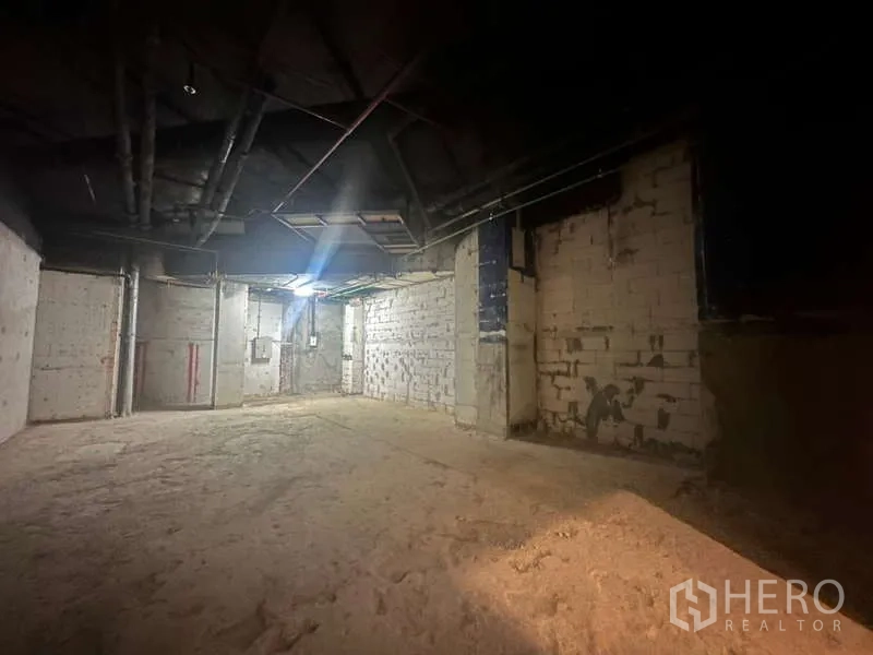 零售空间 出租 - 毛坯角落空间，砌块墙与配电箱清晰可见，顶部单盏灯照明。