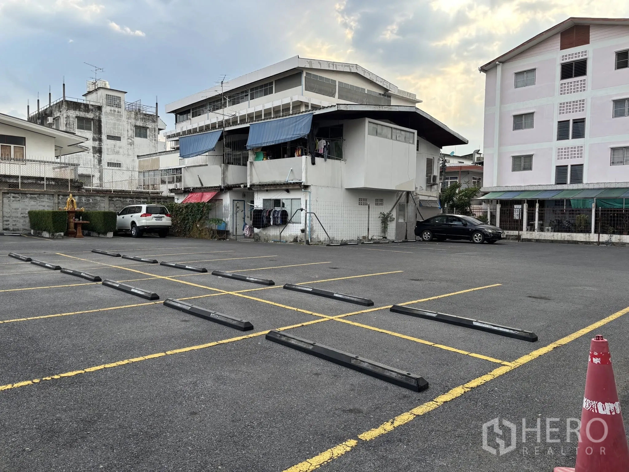 Land for rent in Sathon, Bangkok - Asphalt lot with lined parking spaces beside neighboring buildings and a small shrine by the wall.