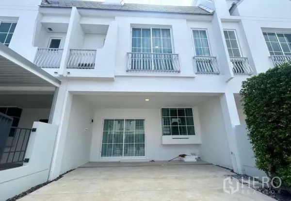 Townhouse for rent in Bang Phli, Samut Prakan - Modern white two-storey townhouse facade with covered carport and sliding glass doors.