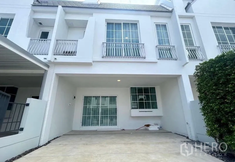 Townhouse for rent in Bang Phli, Samut Prakan - Modern white two-storey townhouse facade with covered carport and sliding glass doors.