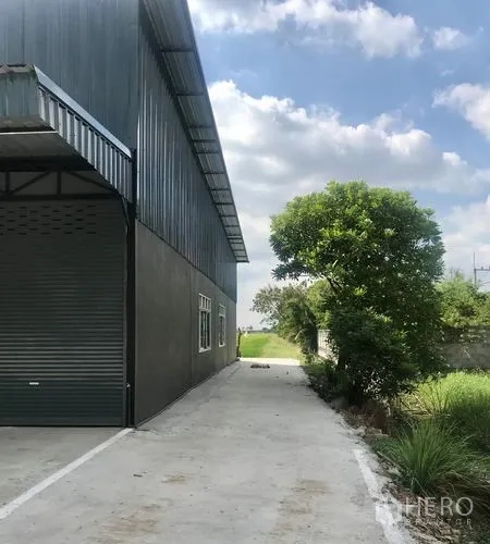 Warehouse for rent in Lam Luk Ka, Pathum Thani - Rear side of the warehouse showing a roller shutter and a long access lane.
