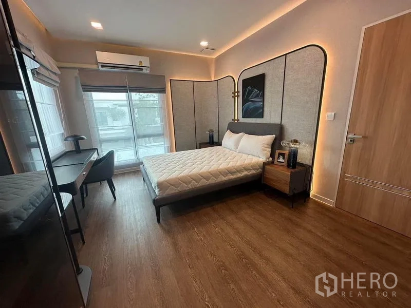 Detached House for rent in Samut Prakan - Upper-floor bedroom with accent wall, balcony doors and desk.