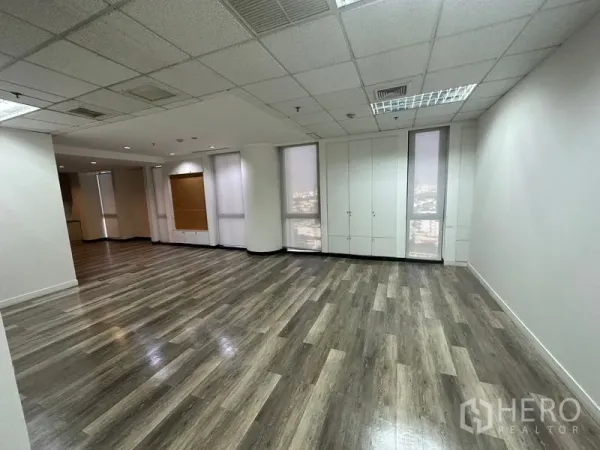 Office Space for rent - Spacious corner workspace with tall windows, roller blinds, built-in storage cabinets and wood-look floors.