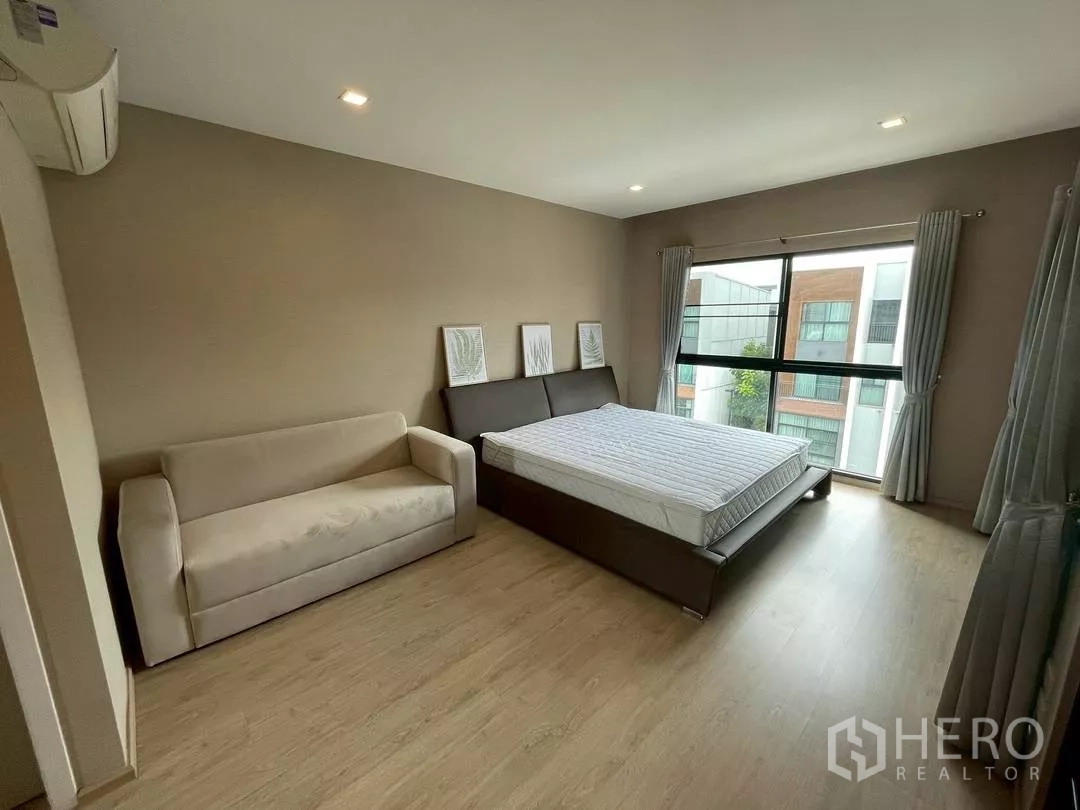 ทาวน์เฮาส์ ให้เช่าในSuan Luang, Bangkok - ห้องนอนมาสเตอร์มีโซฟานั่งเล่น เตียงขนาดใหญ่ และหน้าต่างบานกว้างมองอาคารข้างเคียง.