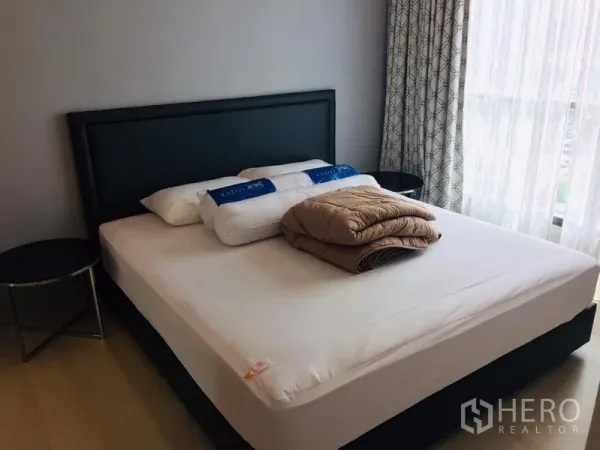 คอนโด ให้เช่าในKhlong Toei, Bangkok - ห้องนอนหลักเตียงใหญ่ หัวเตียงหุ้มหนัง โต๊ะข้าง และหน้าต่างสูงพร้อมผ้าม่าน