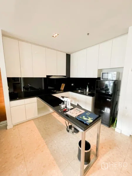 Condominium for rent in Khlong Luang, Pathum Thani - Modern L-shaped kitchen with glossy white cabinets, black countertops and backsplash, and a breakfast bar.