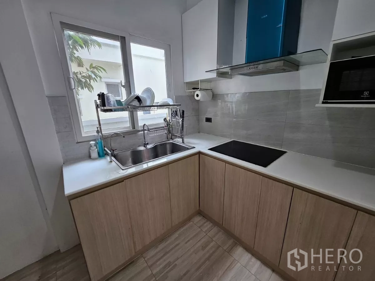 独立式住宅 出租在Khlong Toei, Bangkok - 现代L形厨房，带窗与双槽水槽、电磁炉、抽油烟机与浅木柜体。