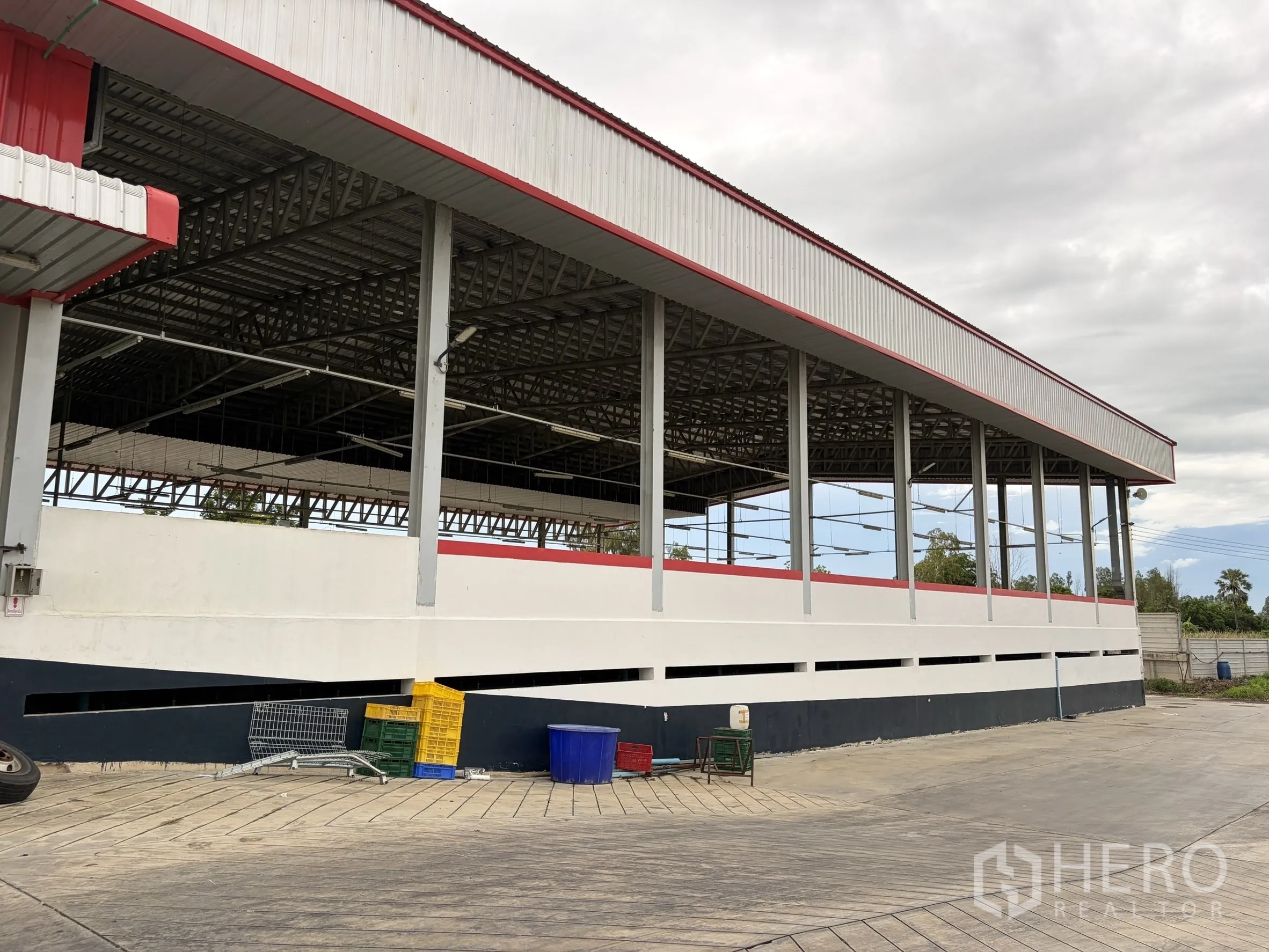 Factory for sale in Mueang Nakhon Pathom, Nakhon Pathom - Open-sided high-roof structure with steel beams and storage crates.