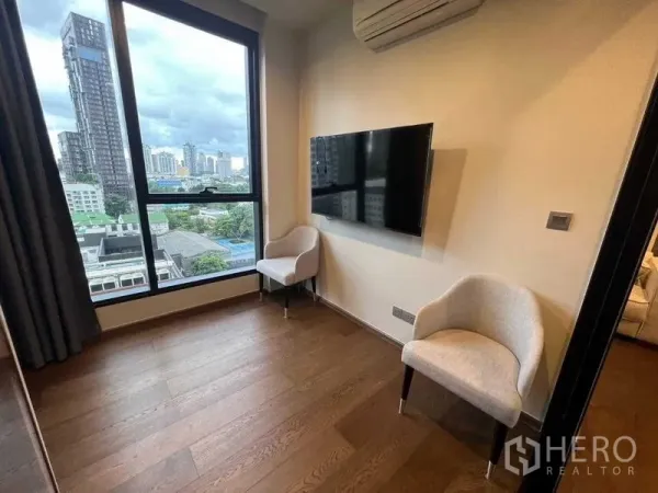 คอนโด ให้เช่าในKhlong Toei, Bangkok - มุมห้องพร้อมเก้าอี้สองตัว ทีวีติดผนัง และหน้าต่างสูงมองเห็นวิวเมือง