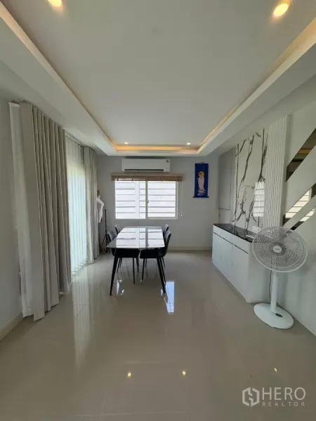 Detached House for rent in Bang Phli, Samut Prakan - Dining room with long table for six, recessed ceiling lights and a marble feature wall near the stairs.