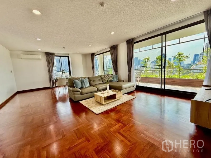Condominium for rent - Living room with L-shaped sofa, panoramic windows, and a balcony overlooking Bangkok.