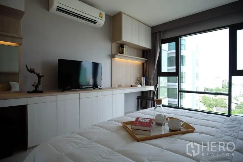 Condominium for rent in Khlong Toei, Bangkok - Bedroom with built-in desk and cabinetry, TV, air-conditioning and corner windows.