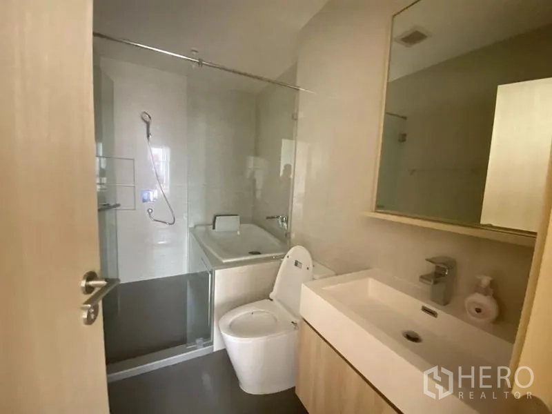 Condominium for rent in Watthana, Bangkok - Second bathroom featuring bathtub with shower screen, vanity with mirror, and toilet.