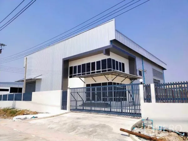 工厂 出租在Samut Prakan - 现代金属板外墙工厂外立面，转角办公窗、滑动铁门、宽混凝土车道与高卷帘门。
