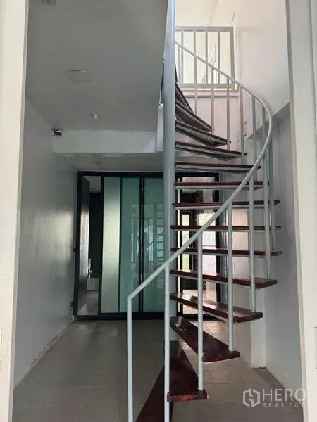 Shophouse for rent in Bang Rak, Bangkok - Metal spiral staircase with wooden treads beside frosted glass sliding doors in a bright corridor.