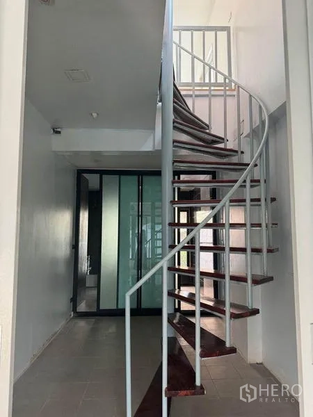 Shophouse for rent in Bang Rak, Bangkok - Metal spiral staircase with wooden treads beside frosted glass sliding doors in a bright corridor.