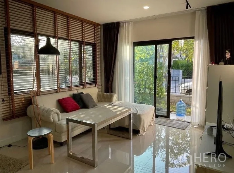 Detached House for rent - Living room with L-shaped sofa and sliding glass doors opening to a small green garden.