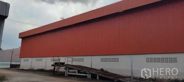货栈 出租在Nikhom Phatthana, Rayong - 橙色金属外墙仓库外观，带装卸坡道和作业场地，位于罗勇尼空帕塔那。