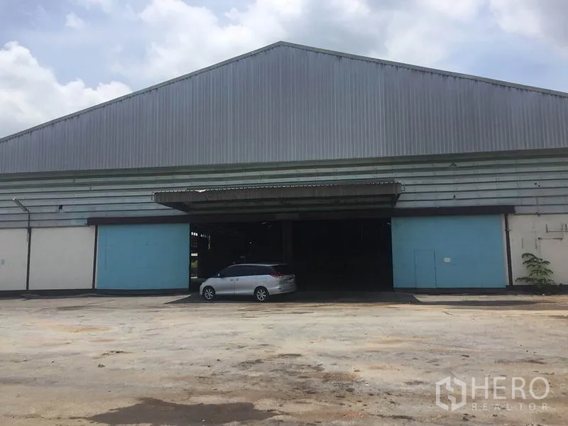 Office Space for rent in Sai Noi, Nonthaburi - Front elevation showing a covered loading bay, blue roller doors and car parking on the forecourt.