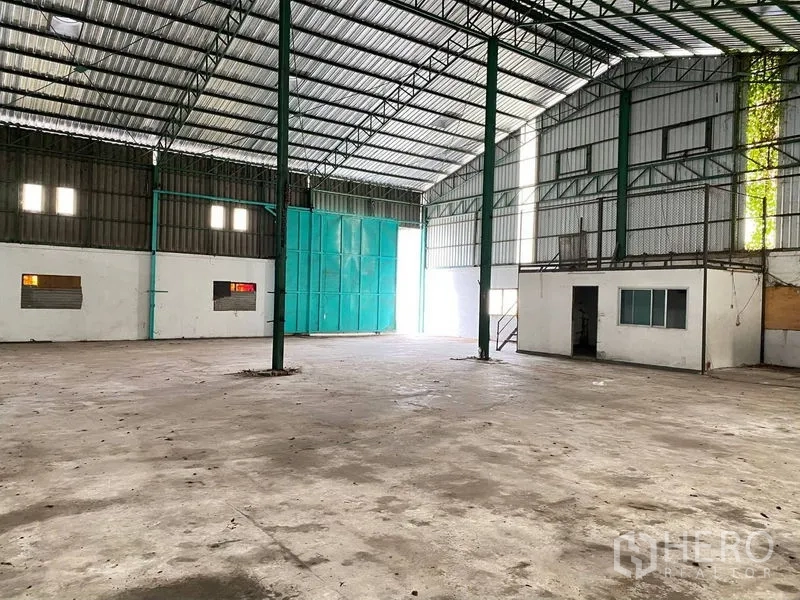 Warehouse for rent in Phra Samut Chedi, Samut Prakan - Open-plan warehouse showing large sliding doors, small office room and bright skylights.