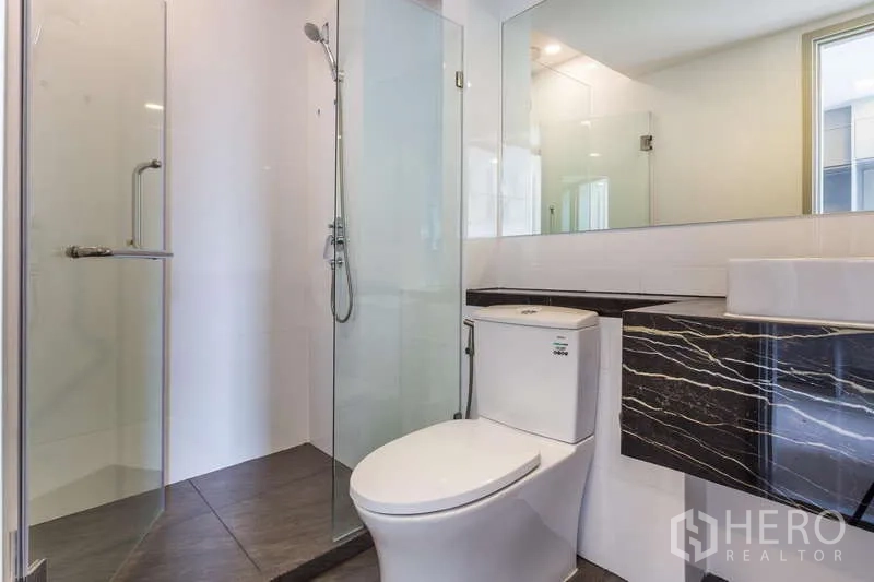 Condominium for rent or sale - Bright bathroom with glass shower enclosure, toilet and black marble vanity.