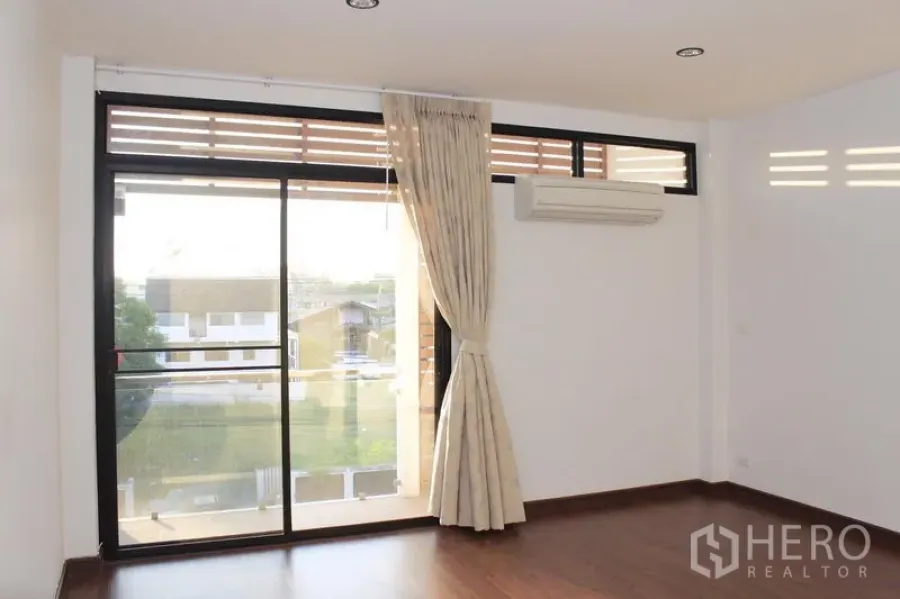 Townhouse for rent in Phaya Thai, Bangkok - Bright upper-level room with sliding glass doors to a balcony, wood floors, and wall-mounted air conditioner in a Phaya Thai townhouse.