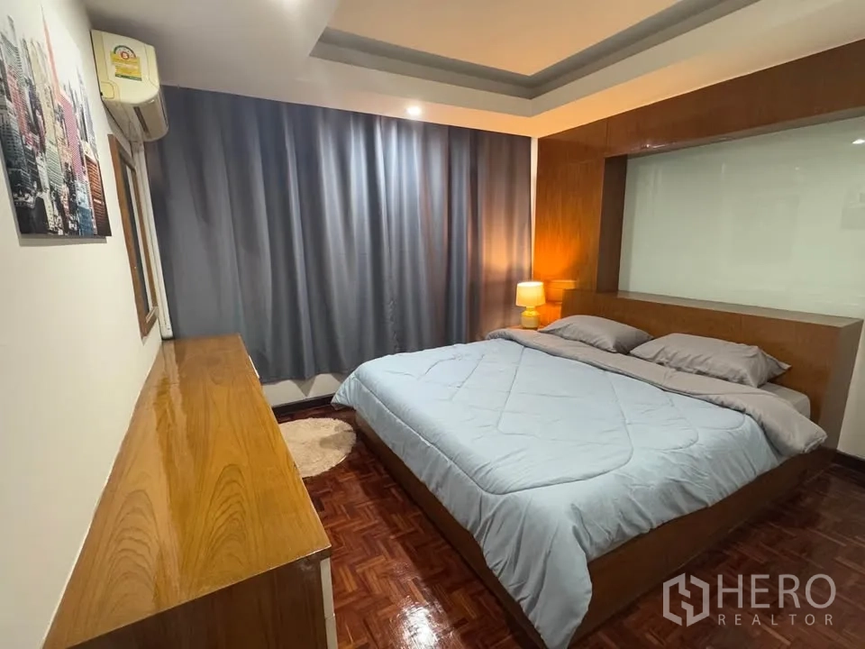 Condominium for rent in Huai Khwang, Bangkok - Third bedroom with double bed, wood built-in headboard, long dresser and soft lighting.