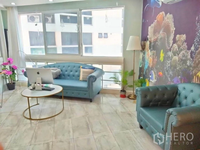 Condominium for rent in Khlong Toei, Bangkok - Bright lounge with big windows, blue sofas and an aquarium-themed feature wall.