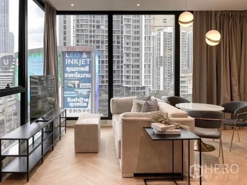 Condominium for rent in Din Daeng, Bangkok - Cozy lounge with beige sofa, TV console and a round dining set beside panoramic windows.