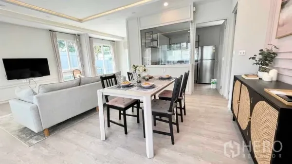 Detached House for rent or sale in Prawet, Bangkok - Open-plan dining area beside living room with wall-mounted TV and glass partition to kitchen.