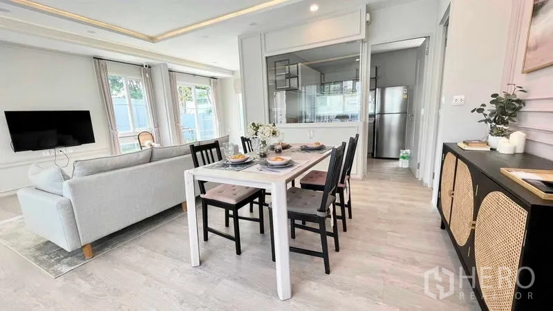 Detached House for rent or sale in Prawet, Bangkok - Open-plan dining area beside living room with wall-mounted TV and glass partition to kitchen.