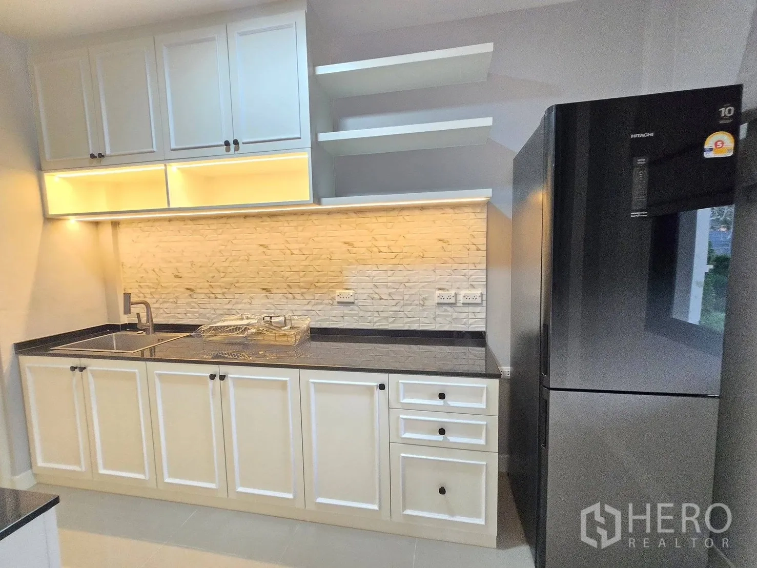 Detached House for rent or sale in Bang Phli, Samut Prakan - Kitchen angle with sink, illuminated backsplash, storage cabinets, and a large refrigerator.