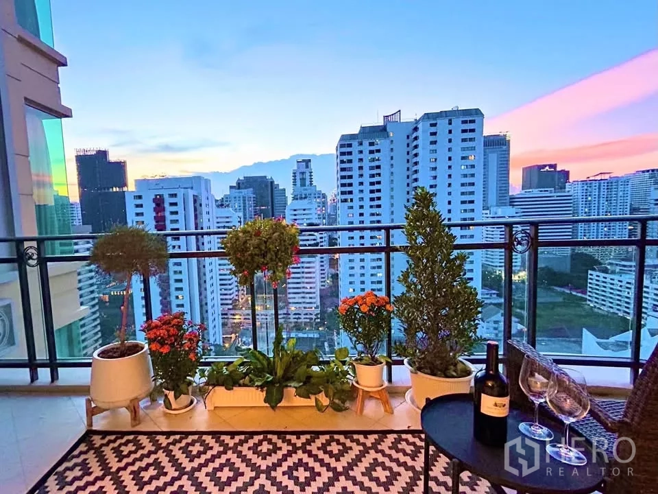 คอนโด ขายในWatthana, Bangkok - วิวเมืองยามเย็นจากระเบียง พร้อมต้นไม้และโต๊ะเล็กจัดแก้วไวน์