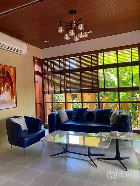 บ้าน ให้เช่าในSuan Luang, Bangkok - ห้องนั่งเล่นสว่างด้วยโซฟาสีกรม เพดานไม้ และหน้าต่างบานใหญ่รับวิวสวน
